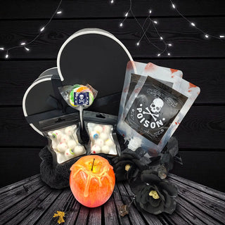 Halloween-themed treats including a bag labeled 'Poison', candy, and an apple on a dark wooden background with string lights.
