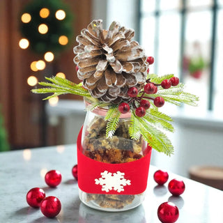 Decorative jar with pine cone, red berries, and greenery on a table with blurred festive background