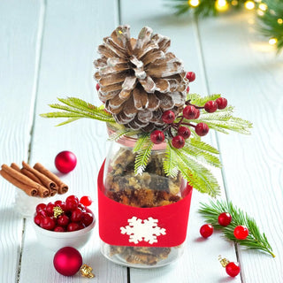 Decorative jar with pine cone, berries, and cinnamon sticks on a light wooden surface.