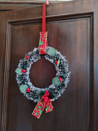 Christmas wreath with red berries and ribbons hanging on a wooden door