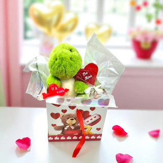 Green teddy bear with heart-shaped cards in a decorative box on a white surface.