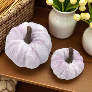 Two white textured pumpkins on a wooden surface with a vase of yellow flowers in the background.