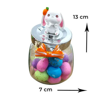 Bunny with a carrot in her hair sitting on a small glass jar with speckled eggs for easter