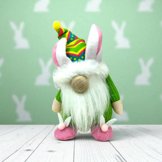 Plush gnome with colorful hat and pink shoes on a wooden floor with a green wall background.