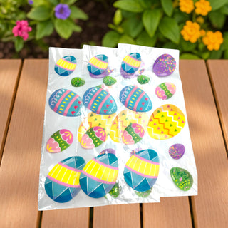 Two packages of colorful Easter egg stickers on a wooden surface with flowers in the background.