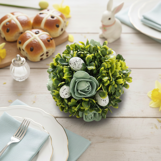 Easter-themed table setting with hot cross buns, a decorative green arrangement, and a rabbit figurine.