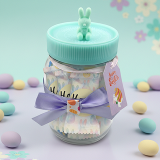 Decorative glass jar with a green lid, rabbit-shaped stopper, and Easter-themed elements on a pastel background.