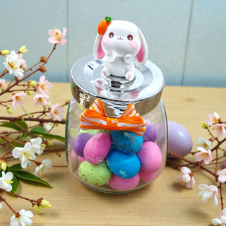 Glass jar with colorful Easter eggs and a bunny-shaped lid on a wooden surface with floral decorations.