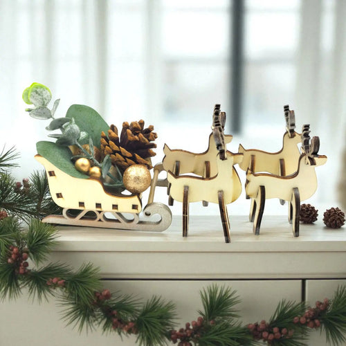 Decorative set with wooden reindeer and a sleigh on a white surface with greenery.