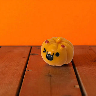 Pumpkin-shaped toy with a face on a wooden surface with an orange background
