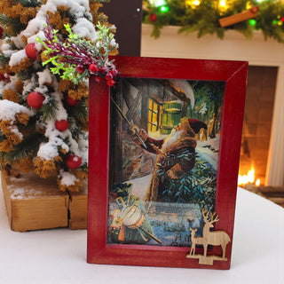 Framed Christmas-themed artwork with a snowy scene and Santa Claus, next to a decorated Christmas tree.