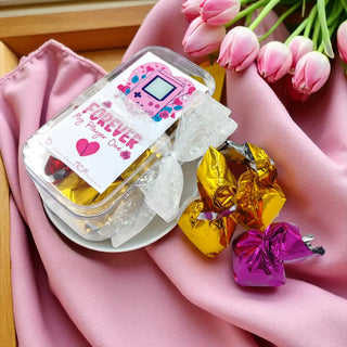 Jar of candy with a decorative label on a pink surface with pink tulips in the background