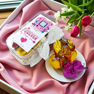 Jar of gold and pink wrapped candies on a pink fabric background with flowers.