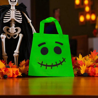 Green Halloween treat bag with a face design in front of a skeleton and autumn leaves.