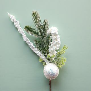 Decorative arrangement with greenery, a white pearl-like branch, and a glittery white sphere on a light green background.