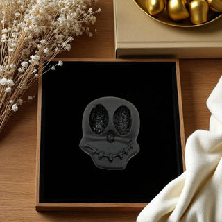 Black skull-shaped object on a dark surface with decorative elements like flowers and gold objects.