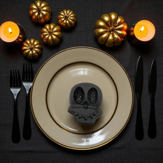 Halloween-themed table setting with skull-shaped object on a plate, gold pumpkins, and candles.
