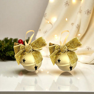 Two gold glittery Christmas bells with bows on a reflective surface with a festive background.