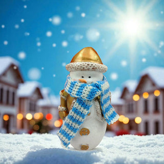 Snowman figurine with a blue and white striped scarf against a snowy village background