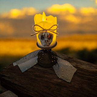 Decorative candle with skull design on a wooden surface during sunset.