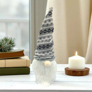 Decorative gnome with a patterned hat next to a candle on a table.