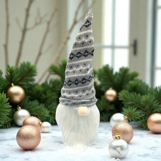 Decorative gnome with a patterned hat surrounded by Christmas ornaments and greenery.