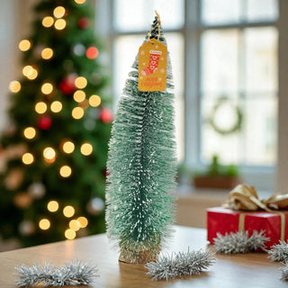 Small decorated Christmas tree with a tag on a table, blurred Christmas tree and gift in the background