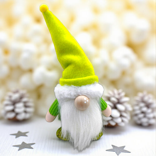 Gnome figurine with a green hat and white beard on a blurred background with pinecones and stars.