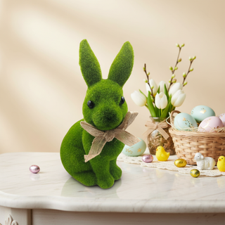 Green moss rabbit with a bow on a decorative table with Easter eggs and flowers.