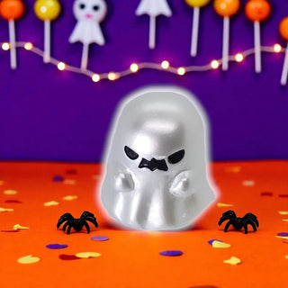 Silver ghost-shaped candy mold on a Halloween-themed background with lollipops and spiders.