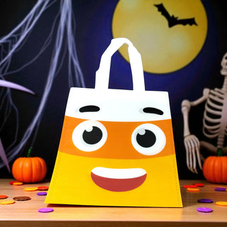 Halloween-themed candy bag with a face design on a table with pumpkins and a skeleton.