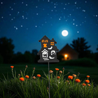 Halloween-themed decorative house light on a grassy lawn with flowers under a night sky.