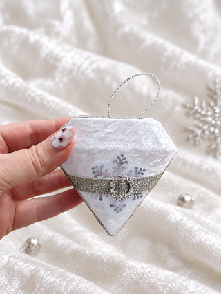Close-up of white velvet diamond ornament with silver snowflake print and silver cord hanger