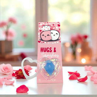 Pink packaging of 'Hugs & Squishes' with a blue squishy toy on a blurred floral background