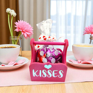 Pink 'Kisses' holder with candy on a table with cups and flowers.