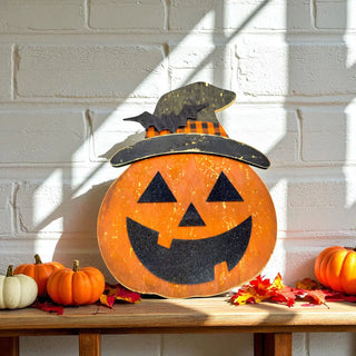 Decorative pumpkin with a witch hat on a wooden table against a white brick wall.