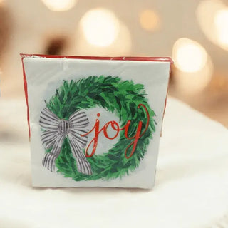 white serviette with green wreath adorned with a black-and-white bow and the word "joy"