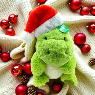Green plush toy with a Santa hat surrounded by red ornaments on a textured surface