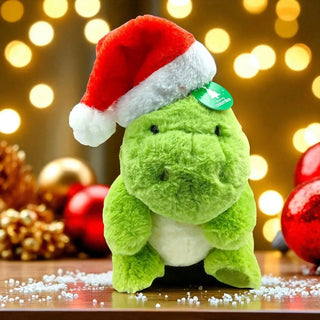 Green plush toy with a Santa hat on a festive background with lights and decorations.