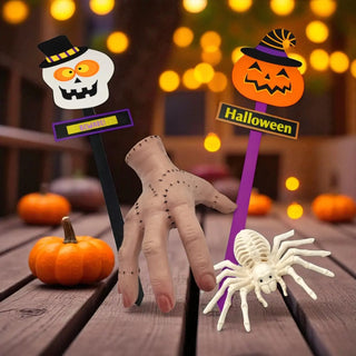 Halloween-themed decorative sticks with a skeleton hand, spider, and pumpkins on a wooden surface.