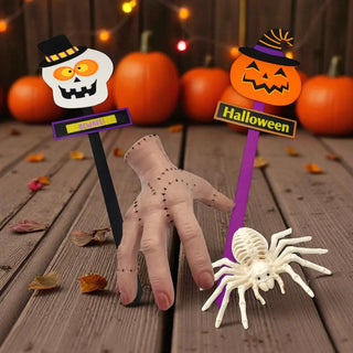 Halloween-themed decorations including a skeleton hand, spider, and jack-o'-lantern on a wooden surface with pumpkins in the background.