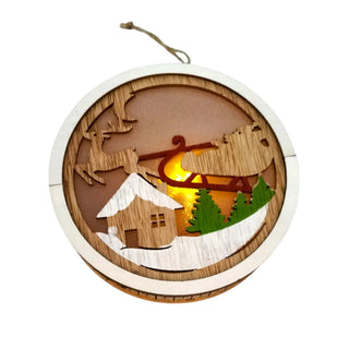 Wooden ornament with a winter scene featuring a house, trees, and sleigh, illuminated from within.