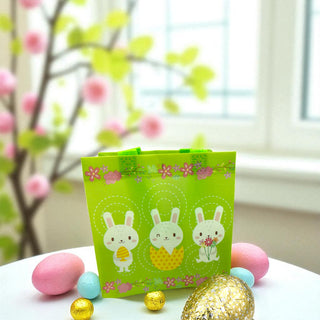 Green Easter-themed gift bag with bunny designs on a table with Easter eggs and decorations.