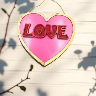 Heart-shaped pink sign with 'LOVE' in red letters on a wooden surface