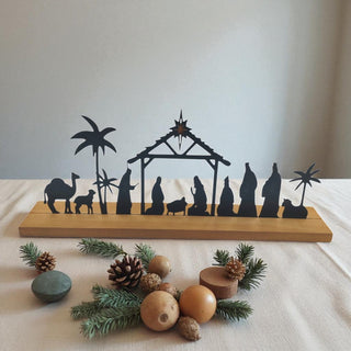 Silhouette nativity scene on a wooden base with decorative elements on a white surface.