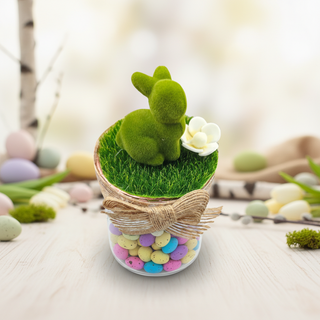 Decorative Easter arrangement with a green rabbit, flowers, and colorful eggs on a light background.