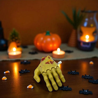 Yellow skeleton hand  on a Halloween-themed table with pumpkins and candles.