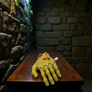 Yellow hand-shaped windup toyon a wooden board against a stone wall.