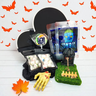 Halloween-themed products including a black cat-shaped container, zombie-themed candy packages, and a yellow rubber glove on a white background with orange bats.