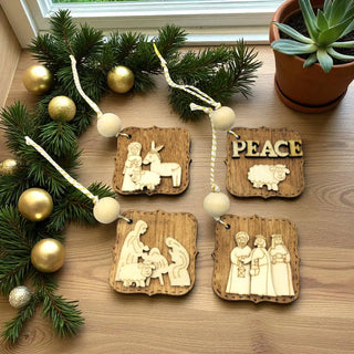 Wooden Christmas ornaments with religious scenes on a wooden surface with greenery and a plant.